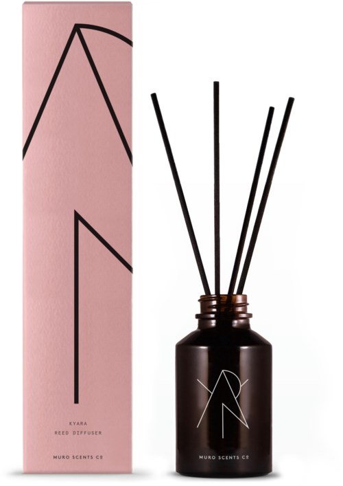 En doftdiffusor med svarta stavar i en mörkbrun flaska, bredvid en rosa förpackning med svarta geometriska linjer.