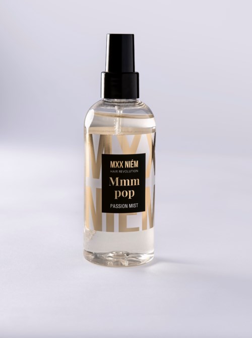 En klar spray i en gennemsigtig flaske med sort sprayhoved og sort og guld label.