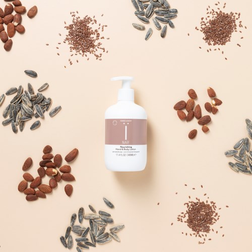 A white pump bottle in the center surrounded by various seeds and nuts on a beige background.