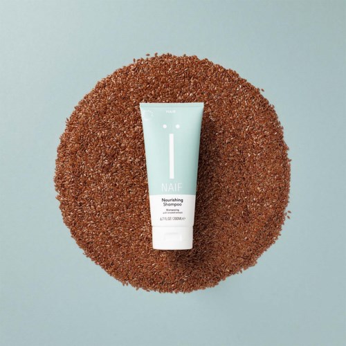 A white tube of NAIF Nourishing Shampoo placed on a round, textured brown mat against a light background.
