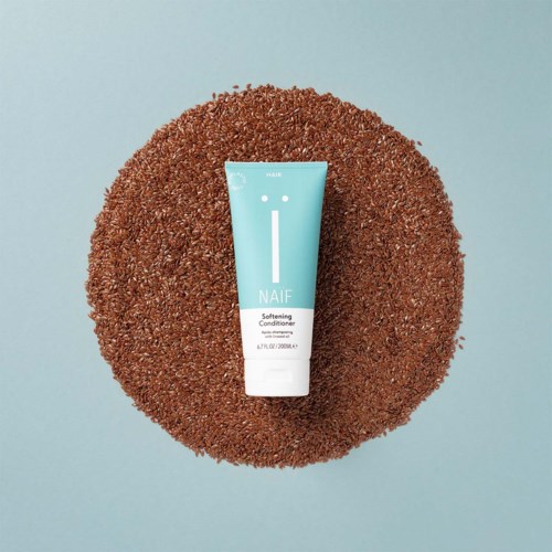 En blå tub märkt 'NAIF Softening Conditioner' på en texturerad brun yta med ljusblå bakgrund.