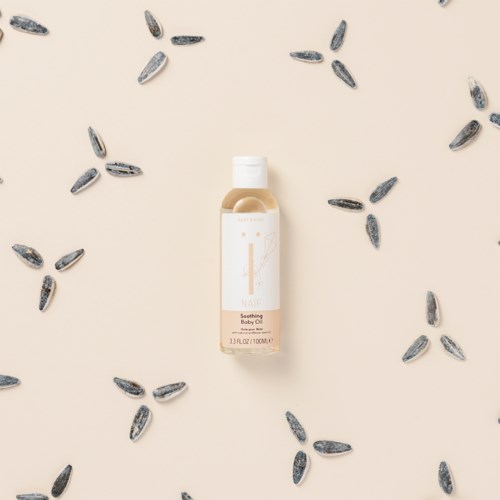 En liten flaska märkt 'Såsande Baby Oil' är omgiven av spridda lavendelfrön på en ljus bakgrund.