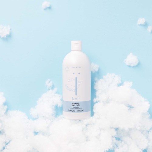 Valkoisen Naïf Relaxing Bath Foam -pullon ympärillä pilviä ja pehmeää puuvillaa. Vaaleansininen tausta. Minimalistinen muotoilu.