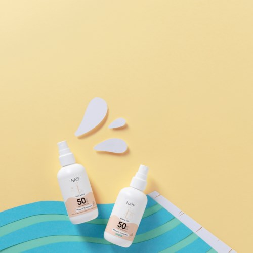 Två flaskor med solkräm med SPF 50 och några droppar på en gul bakgrund, bredvid blå papperlager.