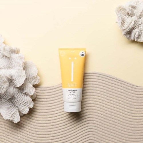 Gul solkremtube med SPF 30, omgitt av koraller og sandtekstur.