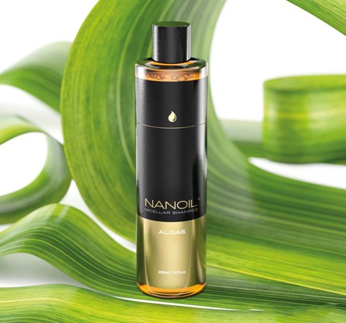 En svart og gull sjamphale merket 'NanoiL Algae' omgitt av store grønne blader.