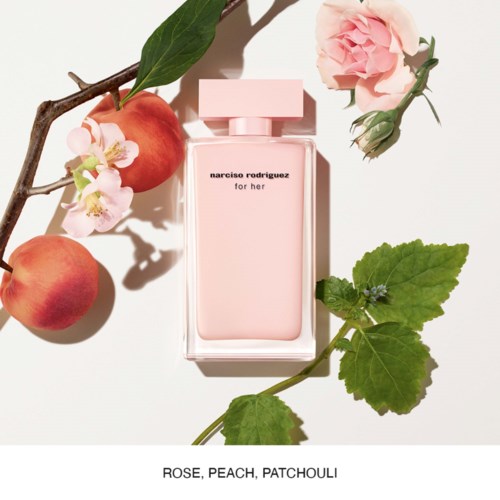 butelka perfum z napisem 'narciso rodriguez for her' otoczona różami, brzoskwiniami i liśćmi oraz kwiatami patchouli.