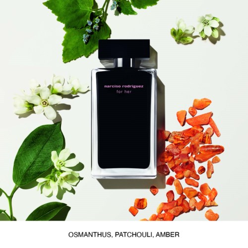 Butelka perfum otoczona zielonymi liśćmi, białymi kwiatami i pomarańczowymi kamieniami, oznaczona 'narciso rodriguez for her.'