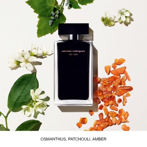 Butelka oznaczona "Narciso Rodriguez for her" otoczona białymi kwiatami, zielonymi liśćmi, bursztynowymi kamieniami i dużym zielonym liściem.