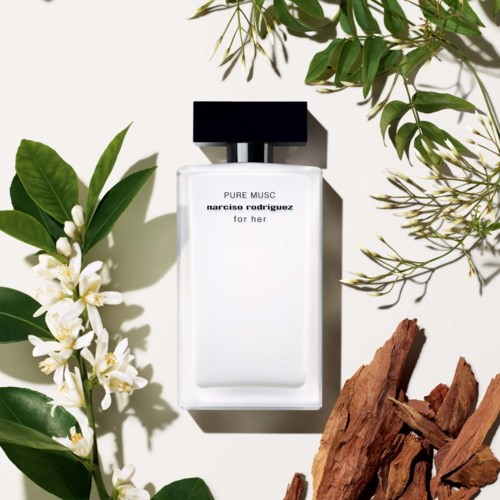 Butelka perfum o nazwie 'Pure Musc' od Narciso Rodriguez, otoczona zielonymi liśćmi, białymi kwiatami i kawałkami drewna.