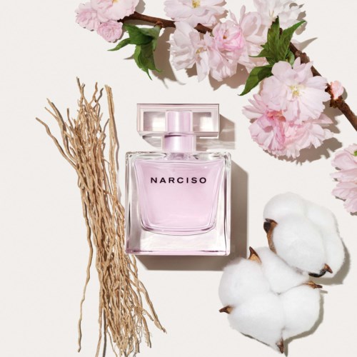 Różowa butelka perfum Narciso z bawełną, suchymi gałązkami i różowymi kwiatami wokół.