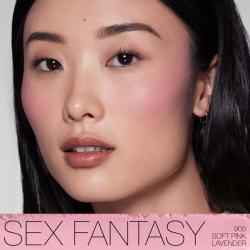 En kvinna med slät hy, mörkt hår och naturlig makeup tittar på kameran, med en rosa banderoll som det står "SEX FANTASY" under.