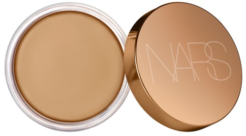 En rund beholder med beige creme indeni og et guld låg med NARS-logo.