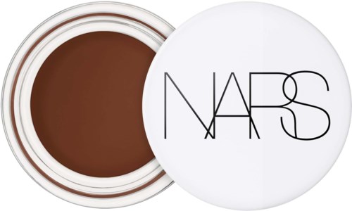 En liten burk med brunt smink eller kräm med vit lock märkt NARS. Locket täcker produkten.