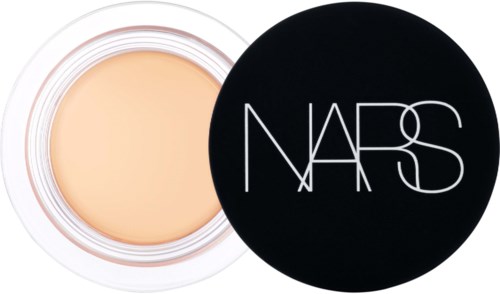 Ein kleines Cremetiegel mit offenem Deckel, das eine beige Kosmetik enthält. Deckel mit NARS-Logo.