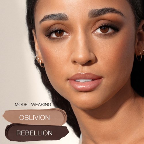 En kvinna med slät hud, smink och örhängen, tittar direkt mot kameran. Text visar smyckesnyanser: Oblivion och Rebellion.