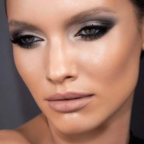 Närbild av en kvinna med mörk ögon makeup, nude läppar och jämn hy.