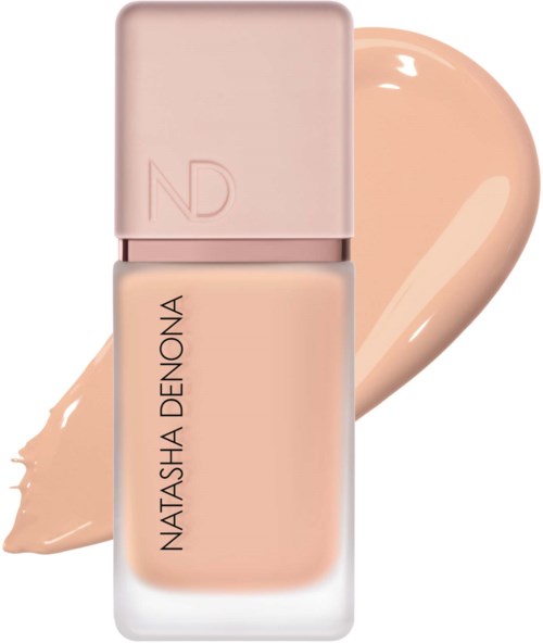 En beige nagellackflaska med rosa kork och varumärket Natasha Denona. Någon nagellack är spritt bakom den.
