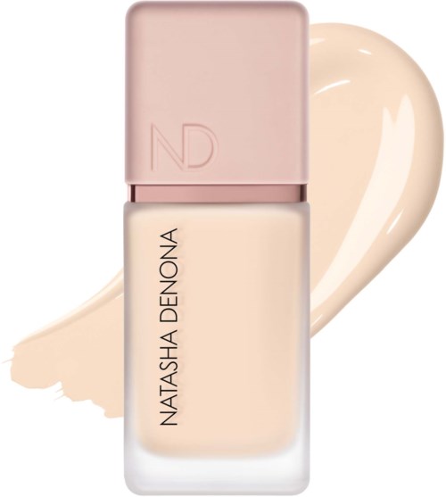 En rosa kork på en vit foundationflaska med Natasha Denona-märke och ett beige färgstänk bakom.