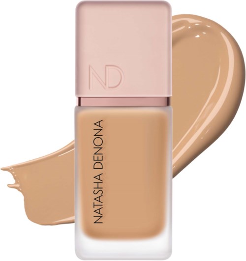 En foundationflaska med en beige kräm bakom, märkt Natasha Denona, med en rosa topp.