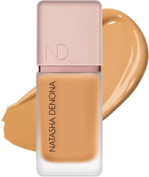 En beige foundationsflaska med rosa lock och Natasha Denona-etikett, med en foundation-svamp bakom den.