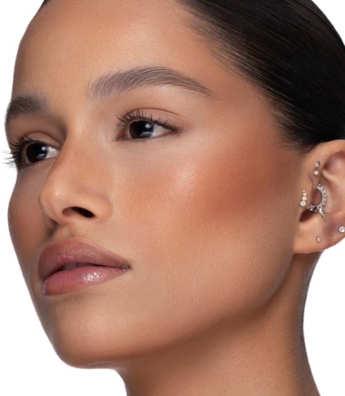 En kvinna med slät hy och mörkt hår, bär flera örhängen och minimal makeup, ser lugn och självsäker ut.