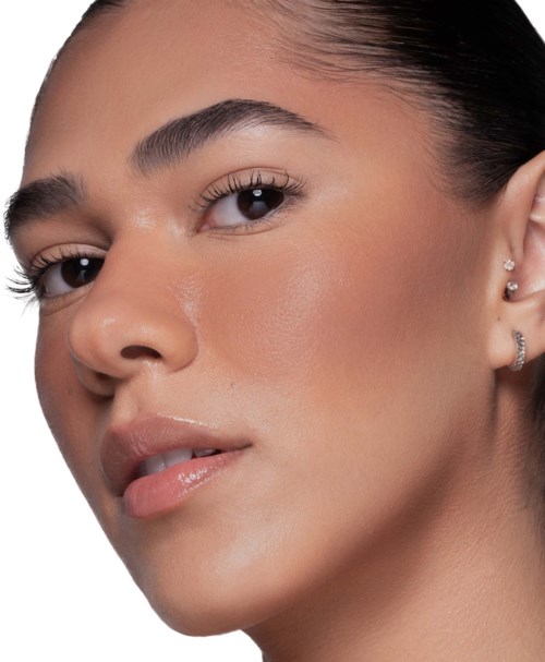 En närbild av en kvinna med slät hud, mörkt hår och naturlig makeup. Hon har örhängen och lätt isatt läppar.