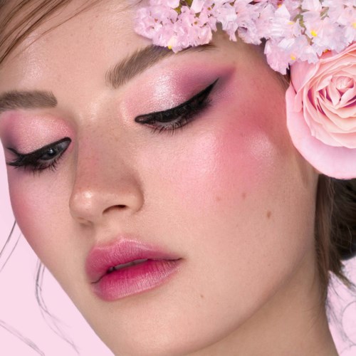 En kvinne med rosa sminke, svart eyeliner og en blomsterkrans av rosa og hvite blomster.
