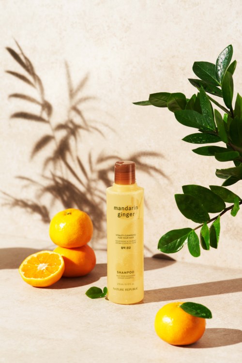 A skincare bottle with oranges and green leaves, casting shadows on a light background.
