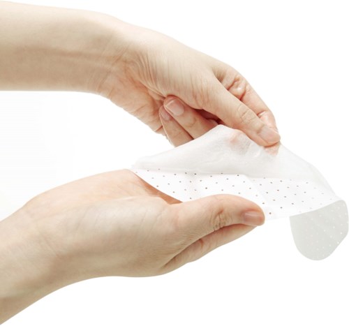 Hands are lifting a white cloth or mask with small dots, showing careful handling.