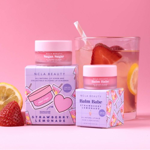 Beauty products and a drink with strawberries and lemons on a pink background.