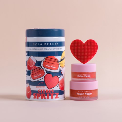 Drei pinke Lippenpflegegläser mit Etiketten, eine rote Herzdekoration und ein blauer Behälter mit Zitronen-Design.