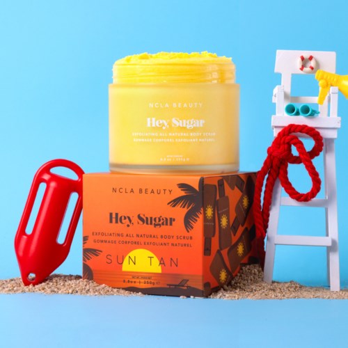 Een gele lichaamscrème, oranje doos met "Hey, Sugar" en zonsondergangontwerp, een rood strand speelgoed, en een blauwe ladder met handdoek.