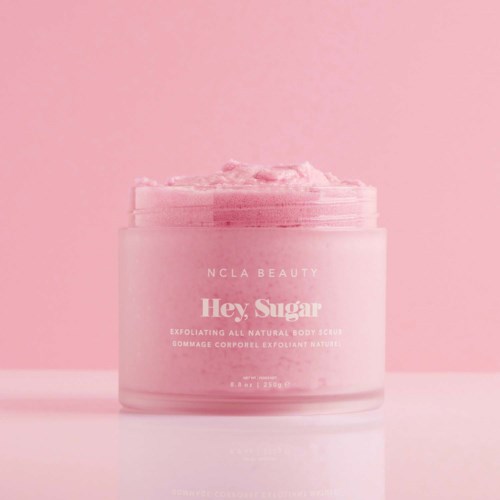 En rosa behållare med kroppsskrubb med vispad textur, märkt 'Hey, Sugar' för exfoliering av huden.