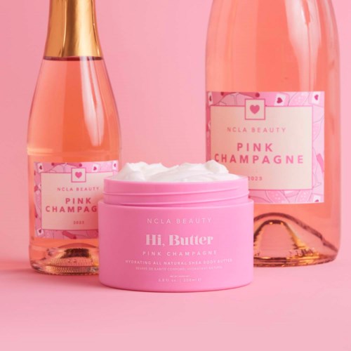 Tre rosa flaskor och en rosa burk med vit kräm, dekorerade med etiketter och ett guldband, på en rosa bakgrund.