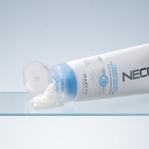 En hvid tube med ansigtscreme med blå accenter ligger med låget af og viser creme, der flyder ud.