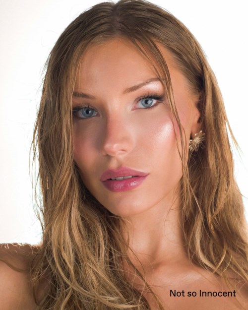 Een vrouw met lang golvend blond haar, blauwe ogen, lichte make-up en een lichte glimlach. Ze draagt oorbellen en een mouwloos topje.