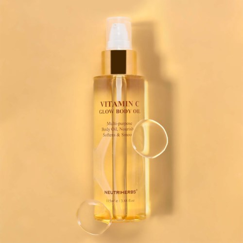 A transparent bottle with golden liquid labeled 'Vitamin C Glow Body Oil' on a yellow background.