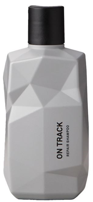 Biała butelka szamponu z geometrycznymi wzorami i czarną nakrętką, oznaczona "ON TRACK REPAIR SHAMPOO."