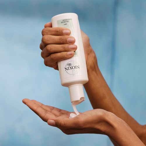 En hand med en flaska lotion eller tvål, med lite utpressat på handflatan, mot en blå bakgrund.