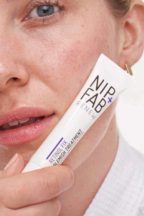 Nærbilde av en kvinne som holder en hudpleieprodukt nær ansiktet, viser del av øyet og leppene. Produktet er merket 'NIP+FAB'.