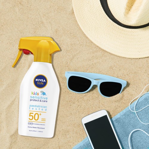 Solskyddsspray, solglasögon, telefon, handduk och hatt på sanden.