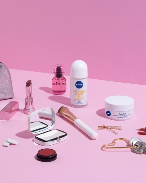 Cosmetic products and accessories arranged on a pink background.