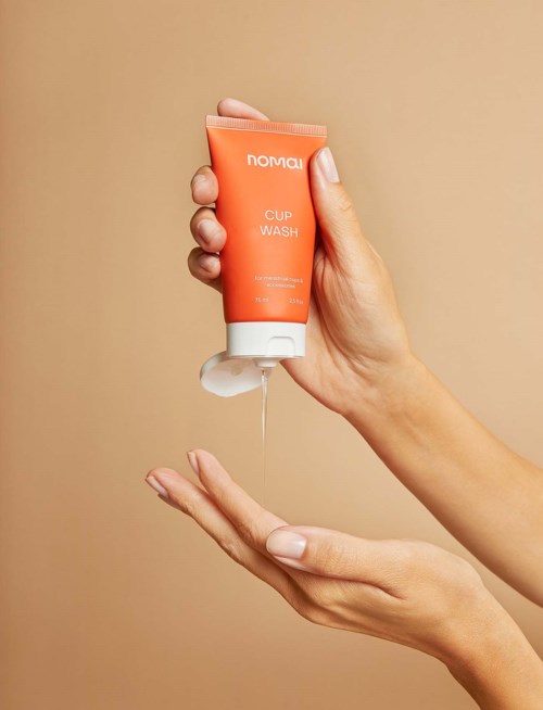 En hånd holder en oransje tube merket 'Nomad Cup Wash' og heller såpe på den andre hånden.