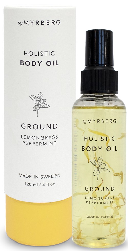 Läpinäkyvä suihkepullo keltaisella öljyllä, valkoisen laatikon kanssa, merkinnällä 'Holistic Body Oil' sitruunasta, häkästä ja piparmintusta.