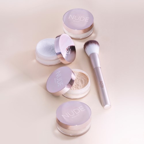 A set of four makeup powders in purple jars and a silver makeup brush on a beige surface.