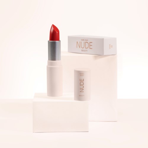 Ett rött läppstift med vit och grå förpackning, placerat på vita block, med en box märkt 'NUDE BEAUTY' i bakgrunden.
