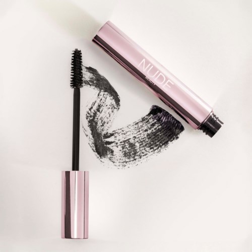 En mascara-børste med svart mascara og en rosa tube merket "NUDE". Mascaraen er spredd på en hvit overflate.