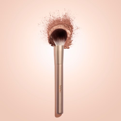 Een make-up kwast raakt blush poeder, verstrooit deeltjes. Eenvoudige achtergrond benadrukt kwast en poeder.