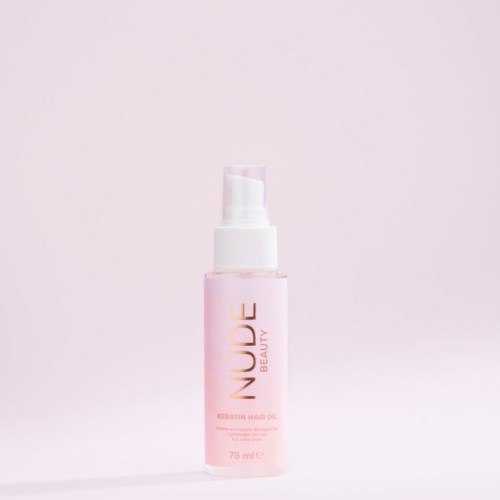 En lyserød flaske mærket "Nuude Beauty Keratin Hair Oil" med pump, på en lys pink baggrund.